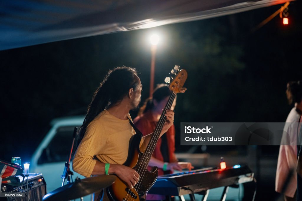 Mid adult man playing a bass guitar in a band at an outdoor music festival Mid adult man playing a bass guitar in a band at an outdoor music festival in Japan Outdoors Stock Photo