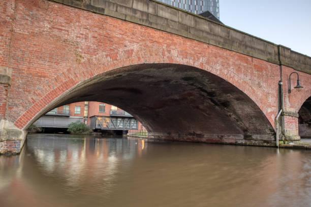 istock Long wide bridge with train line above looking over canal waters below. 1412991935