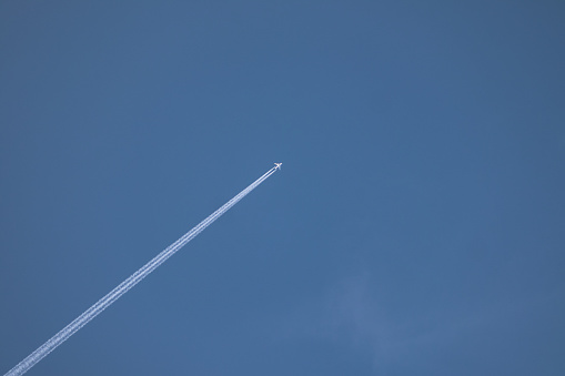 Jet flying high leaving contrail in the blue sky.