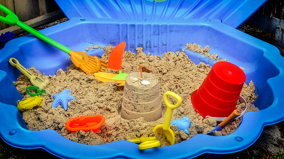 Blue clam shaped plastic sand pit with sand and children’s toys