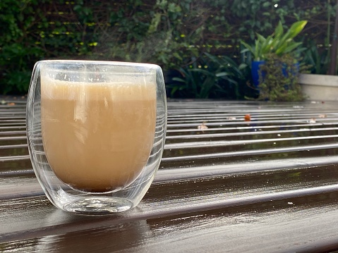 Glass cup of coffee on wet wooden deck