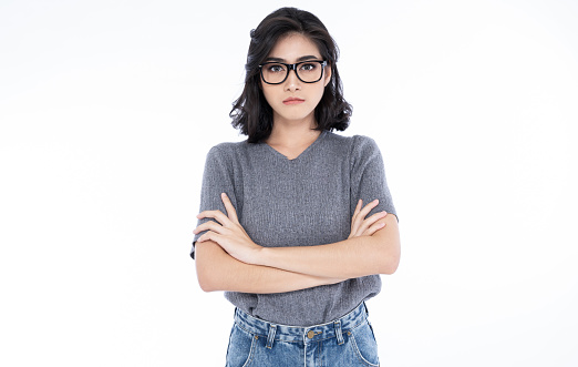 Serious concentrated young Asian woman in eyeglasses posing with crossed arms and looking at camera while standing on isolated over white background. Vision concept.