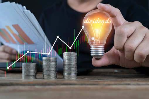 Businessman holding light bulb and virtual graph enhanced by stacking silver coins. Business investment gains and growth in savings and dividends.
