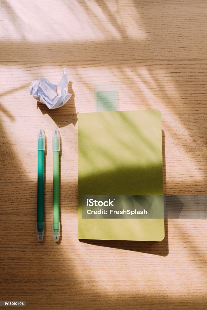 Back To School: A From Above View Of School Supplies Lying On The Desk A close up view of a notebook, two green markers and a piece of crumpled paper on the wooden table. (copy space) Arrangement Stock Photo