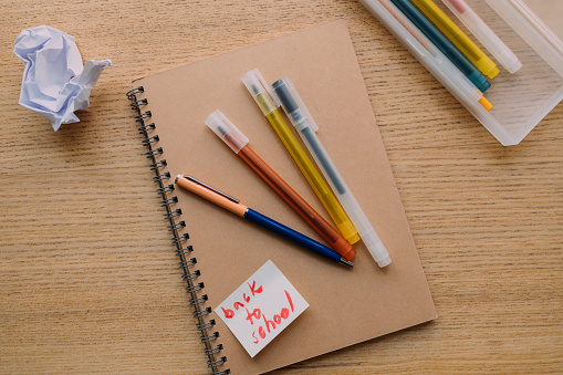 A close up view of a notebook, colourful pens and a piece of crumpled paper on the wooden table. (copy space)