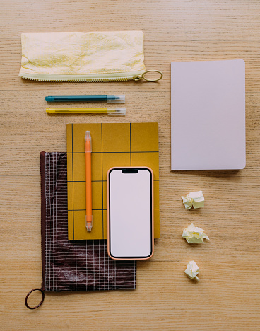 Neatly arranged stationery, pencil cases, some crumpled paper balls and a smartphone on the wooden table. (copy space)