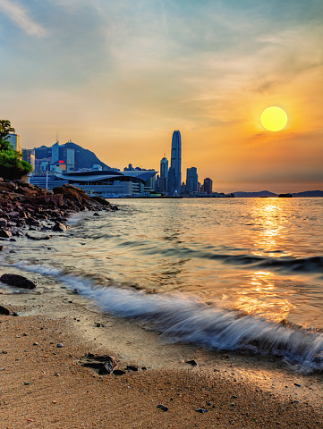 View of Central and Wanchai from the beach of Causeway Bay Yacht Club at sunset. The waves are dazzling, the sun is shining, bright red Victoria Harbour.