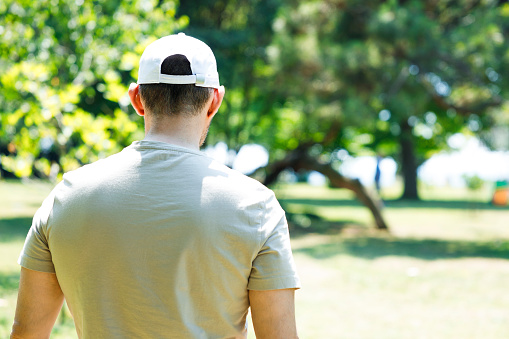Back view of young man wearing a white baseball cap in the park