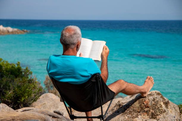 istock Man is reading a book next to the see 1413015639