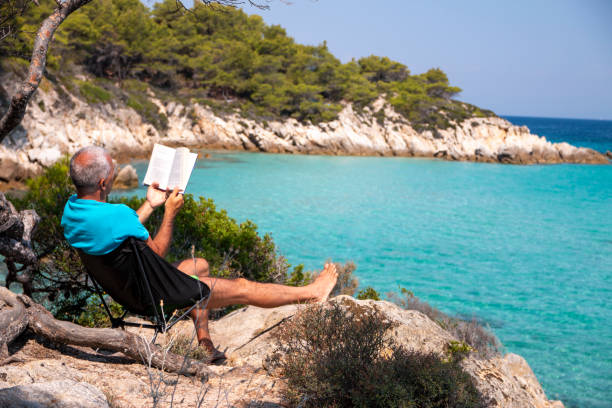 istock Man is reading a book next to the see 1413015641