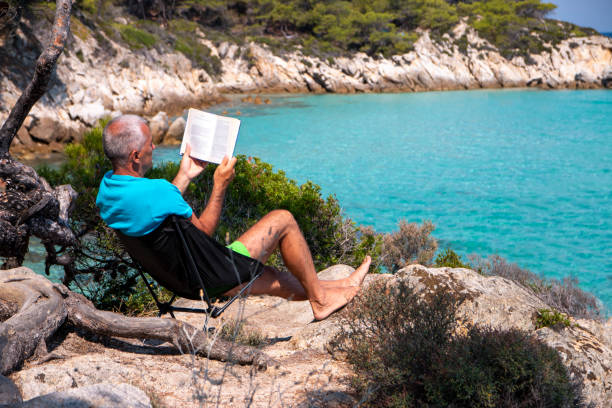 istock Man is reading a book next to the see 1413015644