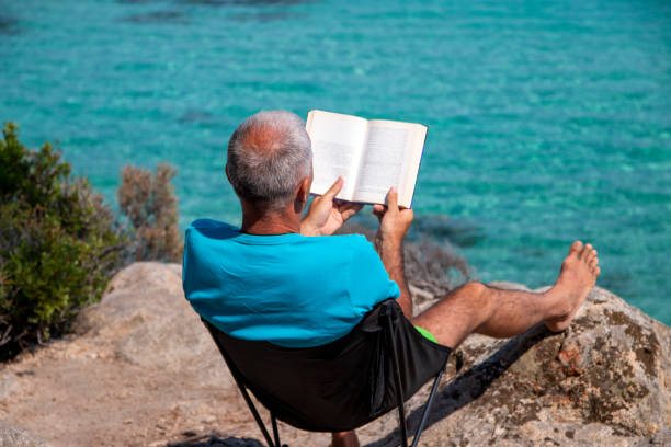 istock Man is reading a book next to the see 1413015646