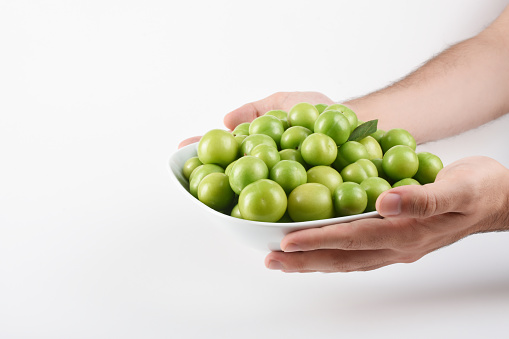 Green plum. Hands holding green plums in the bowl on the white background