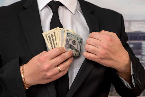 man member or officer in a suit puts a bribe in the form of hundred-dollar bills in his pocket stock photo