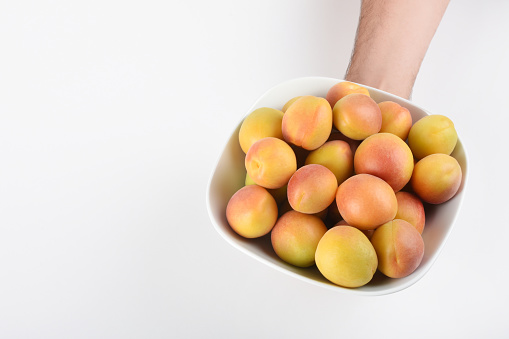 Apricots. Hand holding apricots in the bowl on the white background