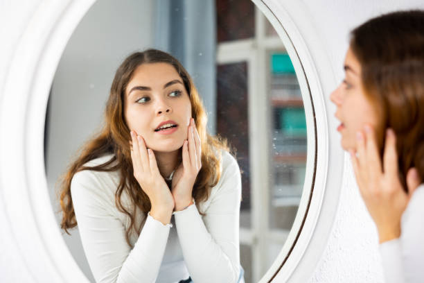 istock Young woman looking at face in mirror 1413020503