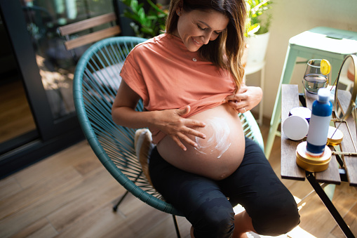 Pregnant woman applying moisturizer on her stomach and enjoying every moment of it.