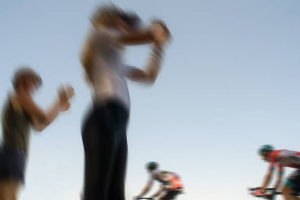 Two blurred people applaud two passing tour de france cyclists