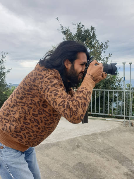 istock Side view of a Indian long haired and bearded young man taking photo with camera while standing outside 1413026947