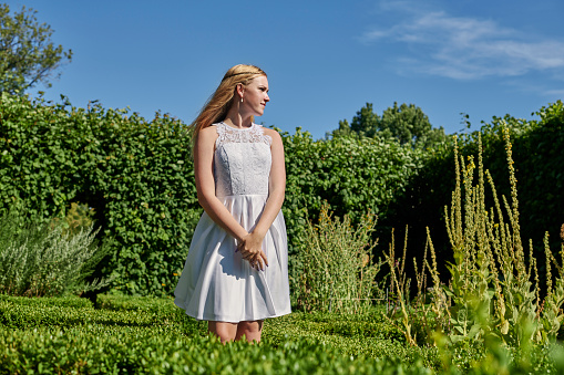 Fourteen year old girl in her official white confirmation dress standing outside in a garden