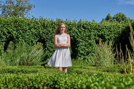Fourteen year old girl in her official white confirmation dress standing outside in a garden