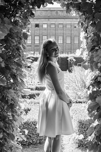 Fourteen year old girl in her official white confirmation dress standing outdoors in romantic garden. Protestant confirmation