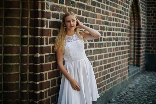 Fourteen year old girl in her official white confirmation dress standing outdoors outside the church