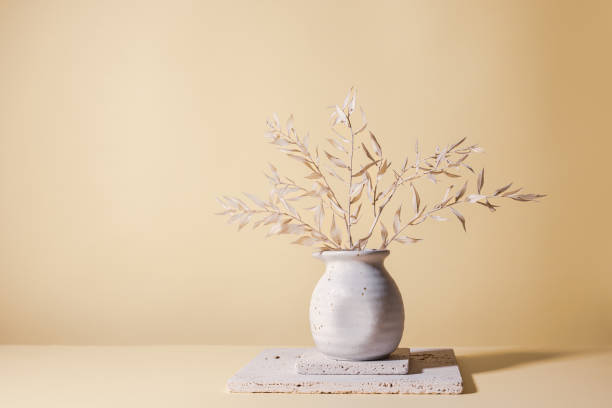 istock Still life with white dried branches with leaves in light ceramic vase on stone blocks on pastel background. Home decoration with dried flowers. 1413031858