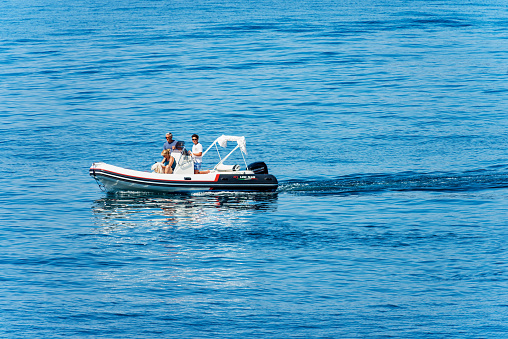 La Spezia, Italy - July 19, 2022: Small motorized dinghy with a family on board (two men, a woman and a dog), on a sunny summer day in the blue Mediterranean sea, Tellaro, Lerici municipality, Gulf of La Spezia or Gulf of Poets, Liguria, Italy, southern Europe.