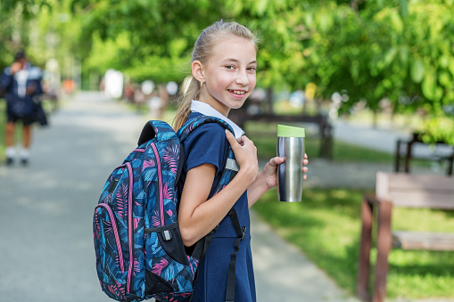 Smiling schoolgirl preteen goes to school with backpack and drink. Concept of back to school, education and childhood.