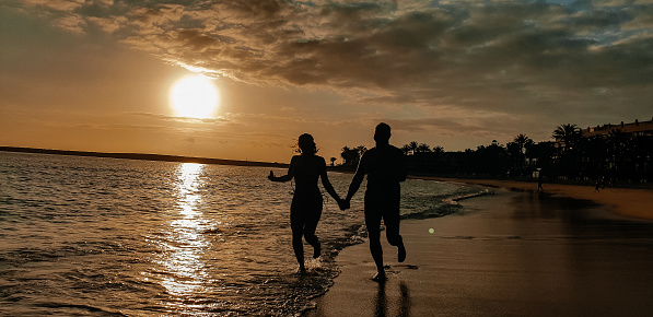 Silhouette of two people by the sea. Happy young couple on a walk by the sea at sunset. Travel and vacation concept. Watch the sunset on the ocean.