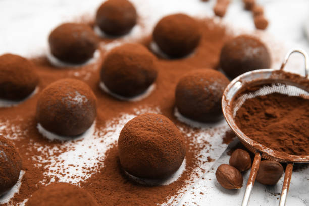 Delicious chocolate truffles with cocoa powder and hazelnuts on white table, closeup Delicious chocolate truffles with cocoa powder and hazelnuts on white table, closeup chocolate truffle making stock pictures, royalty-free photos & images