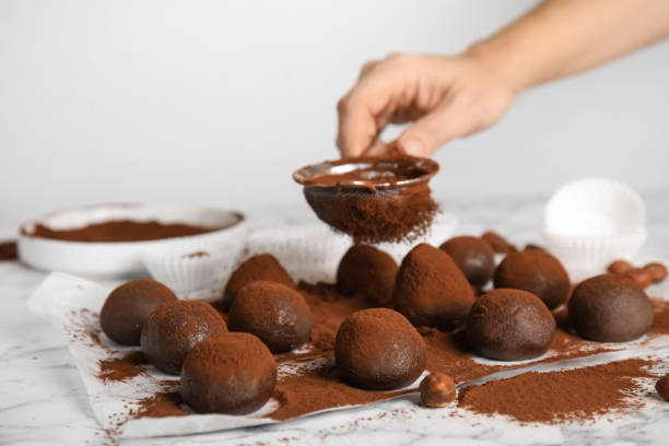 Woman sieving cocoa powder onto delicious chocolate truffles at white marble table, closeup Woman sieving cocoa powder onto delicious chocolate truffles at white marble table, closeup chocolate truffle making stock pictures, royalty-free photos & images