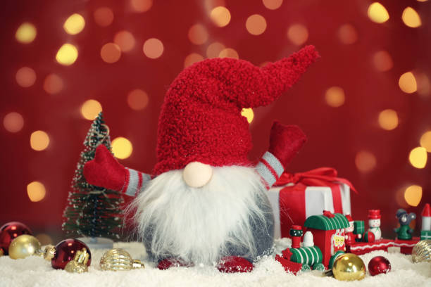istock Cute Christmas gnome, gift box and festive decor on snow against blurred lights 1413038167