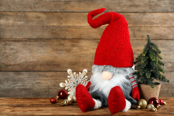 istock Cute Christmas gnome and festive decor on table against wooden background. Space for text 1413038580