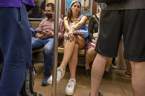 Manhattan, New York, NY, USA - June 26, 2022: Young woman sitting in a crowded subway car on a hot summer day