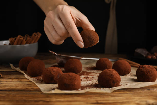 Woman preparing delicious chocolate truffles at wooden table, closeup Woman preparing delicious chocolate truffles at wooden table, closeup chocolate truffle making stock pictures, royalty-free photos & images