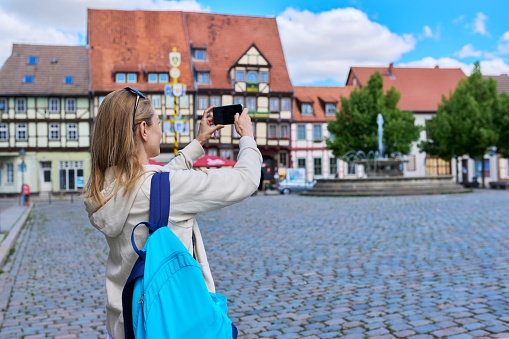 Woman tourist taking photo in an old European city, in front of historical building. Female traveling through Germany using smartphone to take photo. Tourism, history, architecture concept