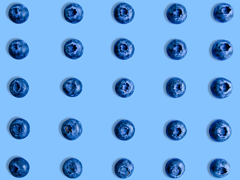 Creative summer layout made of blueberries on bright blue background. Original blueberry decoration. Minimal summer concept. Welcome summer. Copy space. Fruit mosaic.