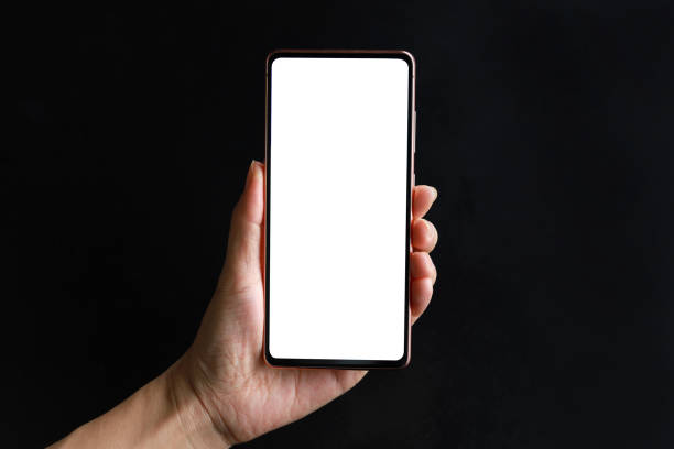 Cropped shot of a woman's hand holding up a smartphone with blank white screen against black background stock photo