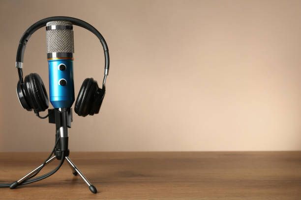 istock Microphone and modern headphones on wooden table against beige background, space for text 1413042115