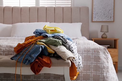 Messy pile of dirty clothes on indoor bench in bedroom. Tidying up method