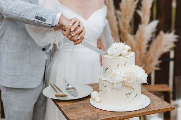 신부와 신랑이 결혼식 연회에서 아름다운 웨딩 케이크를 자르고 있습니다. 손은 섬세한 흰 꽃으로 케이크를 자른다. - honeymoon color image horizontal setting the table 뉴스 사진 이미지