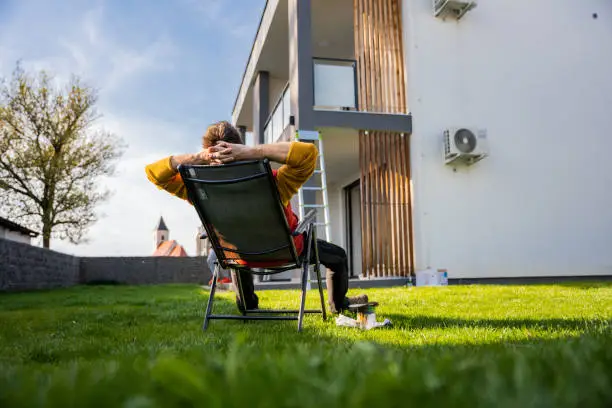 Photo of Tired man relaxing on comfortable chair by equipment in yard outside apartment