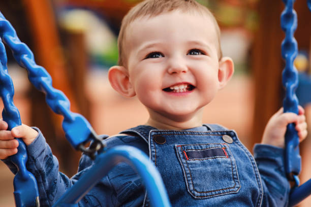 彼の顔に笑顔の幸せな子供スイング、クローズアップ、1歳の幼児の赤ちゃん - playground cute baby blue ストックフォトと画像