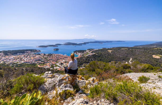 woman sitting on rock and enjoying view of town from top of mountain - sky sea town looking at view imagens e fotografias de stock