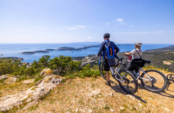 male and female biker with bicycles enjoying view of town from top of mountain - sky sea town looking at view imagens e fotografias de stock