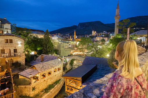 Female tourist looking at beautiful view of old famous houses with minarets against blue sky at dusk