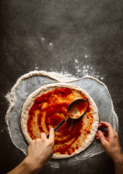 fare una pizza spreding salsa di pomodoro sull'impasto - sugo pronto foto e immagini stock