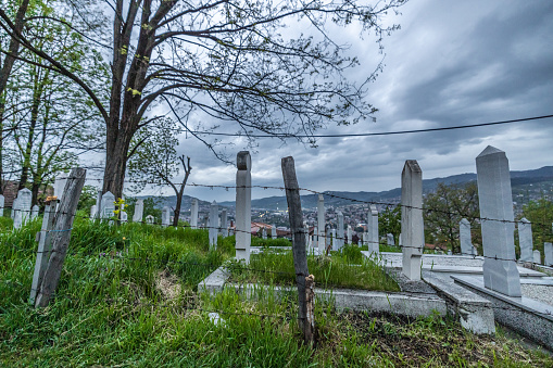Barbed wire fence at the edge of cemetery with tombstones on hill against cloudy sky